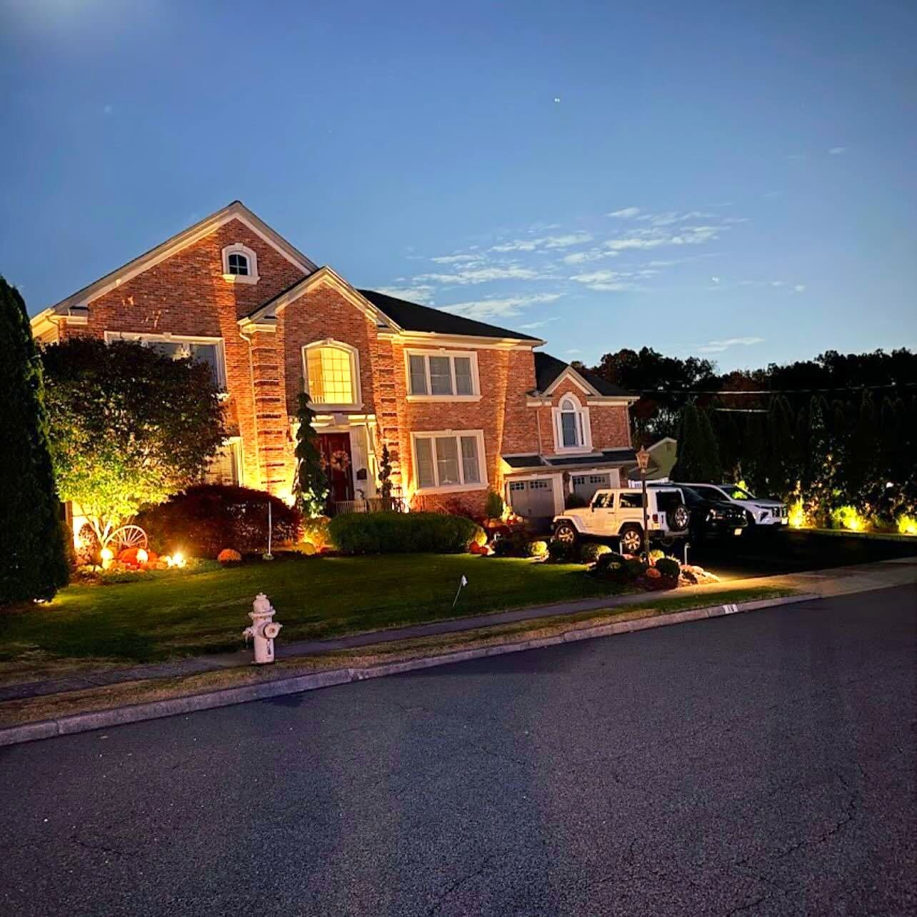 Brick colonial at dusk with warm white landscape lighting washing the facade