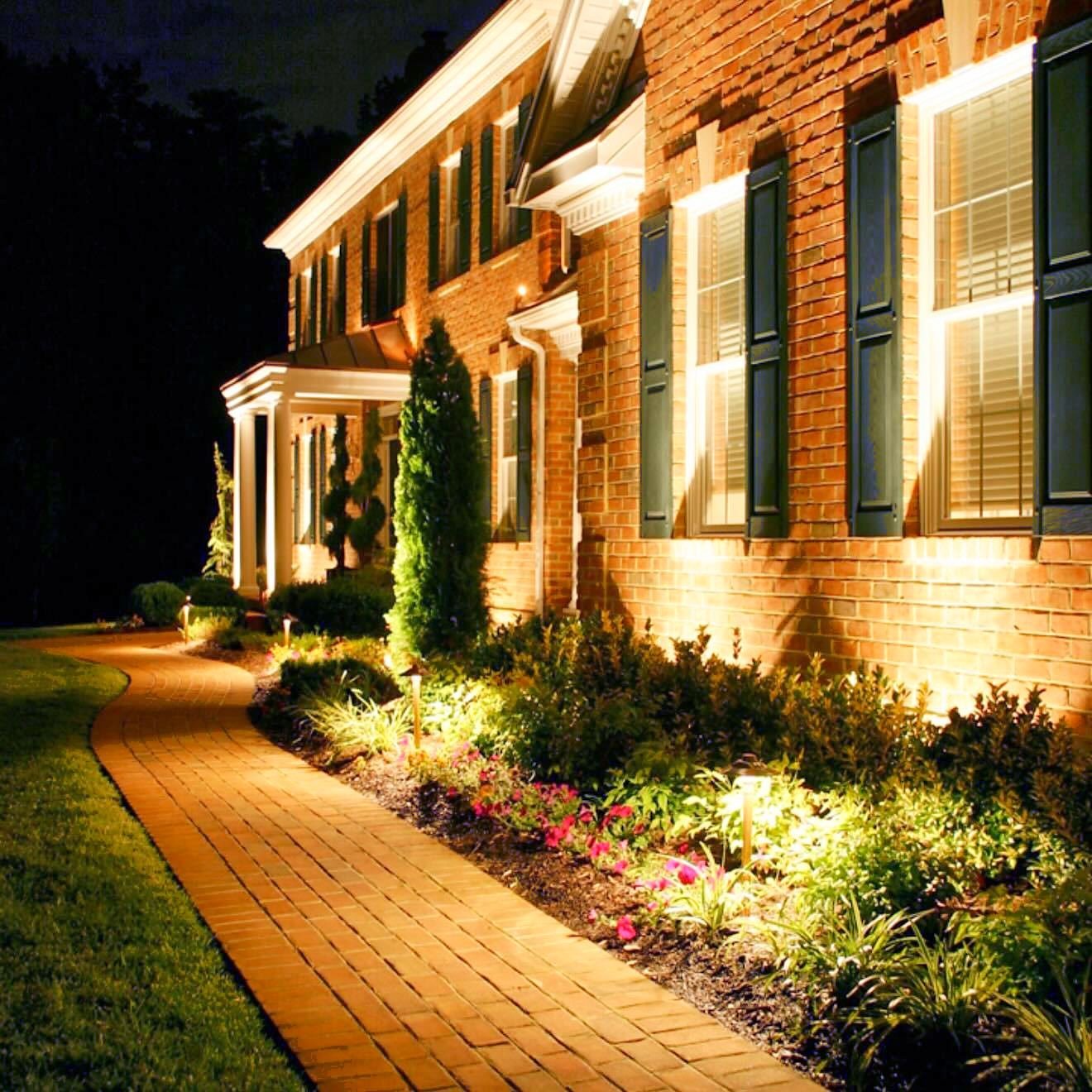 Brick colonial with uplights on the facade and path lights spaced along the walkway